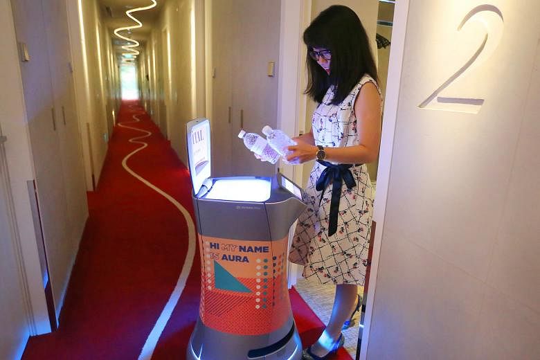 Aura the robot delivering bottled water to a hotel room at M Social Singapore. The robot is able to find its own way around the hotel to deliver room amenities to guests. At the hotel, one robot can do the work of two to three people, and takes an av