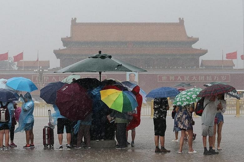 Tourists visiting Tiananmen Square in Beijing yesterday held umbrellas as heavy rain fell. Thunderstorms lashed the Chinese capital yesterday, disrupting hundreds of flights at the city's airport, one of the largest airports in the world. Other airpo
