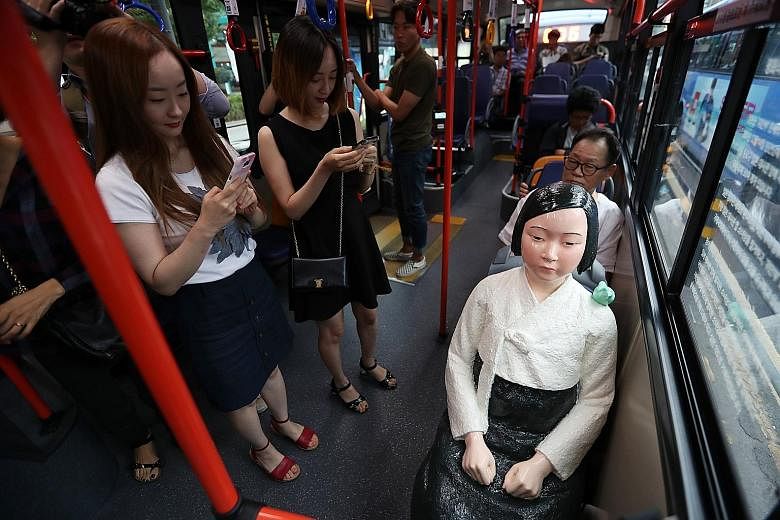 Passengers taking photos of a comfort woman statue installed on a city bus in Seoul yesterday, during the International Memorial Day for Comfort Women. A bus operator installed five comfort women statues on board its buses, and they are slated to rem