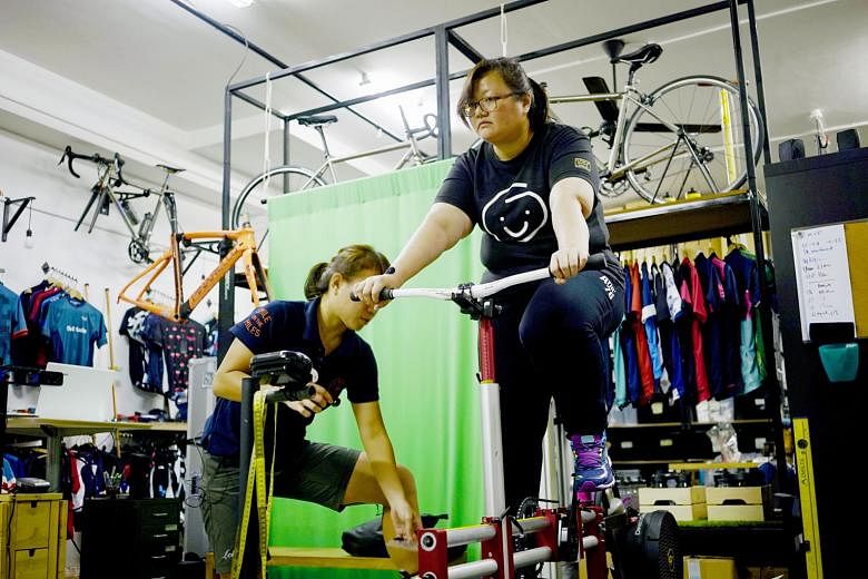 Graphic designer Christine Lim pedalling on a stationary adjustable bicycle jig as Shuwie Chang, sports scientist and bike fitter at Loue Bicycles, makes adjustments after checking her pressure distribution results.