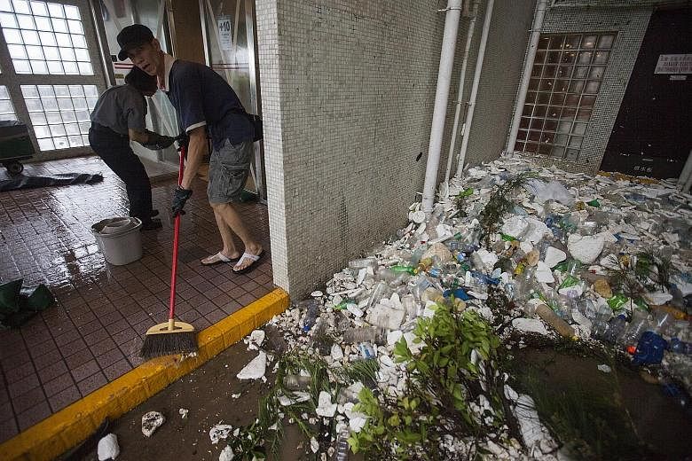 A satellite dish was blown off a rooftop onto the sidewalk in Tsim Sha Tsui, Hong Kong, yesterday. Residents cleaning up the debris at a public housing estate in the district of Heng Fa Chuen, in Hong Kong, after Typhoon Hato swept across the city ye