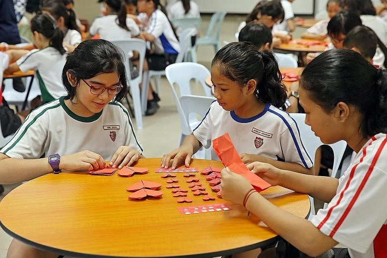 Xishan Primary School pupils (from left) Nur Sarah, 11, Amelia Umairah, 11, and Shahirah Ibrahim, 12, folding paper hearts along with their peers yesterday for the Fold-A-Heart project. For every heart folded and deposited into an SG Cares box, HSBC 