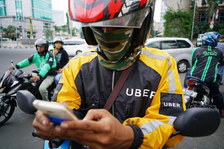 An Uber rider checks his smartphone as a Go-Jek rider (left) ferries a passenger in the background and a GrabBike rider navigates traffic in Jakarta, Indonesia. Asean countries can use digitisation and Internet technology to improve energy and resource us
