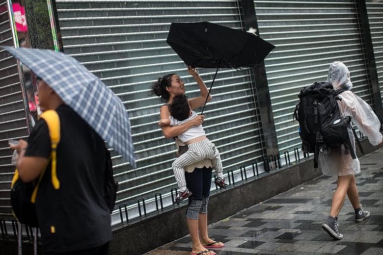Pedestrians in Hong Kong's Tsim Sha Tsui area yesterday coping with rain and wind caused by tropical storm Pakhar. Hong Kong and Macau raised a Typhoon 8 signal early yesterday but lowered it to No. 3 by the afternoon.