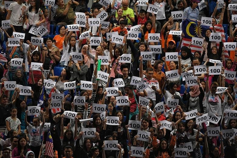 Spectators holding signs with "100" printed on them after rhythmic gymnast Amy Kwan won Malaysia's 100th gold at these Games.