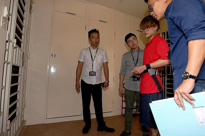 Joven Bey Ding Hui (in red), 16, being accompanied by police officers to a flat in Redhill. He is suspected of setting fire to the front door of three homes in Redhill, Paya Lebar and Bedok. He is also believed to be responsible for loan-shark harass