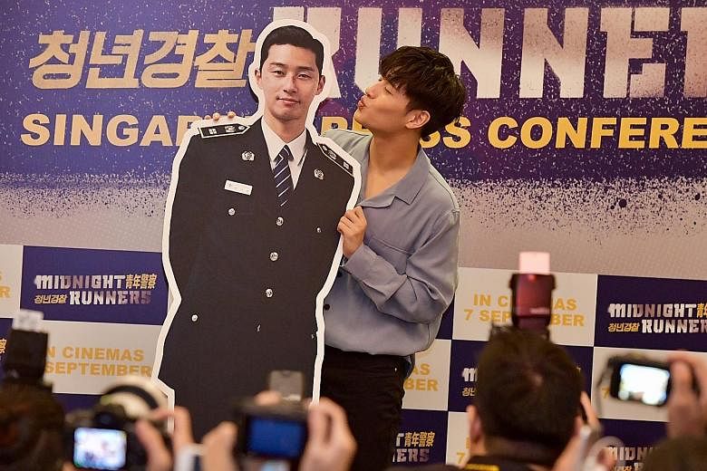 Kang Ha Neul playfully puckering up to his co-star Park Seo Joon's standee at the press conference for Midnight Runners.