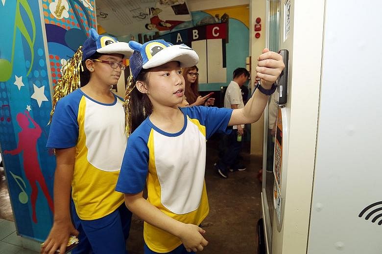 Pupil Vernice Lim, 11, using her smartwatch at a vending machine to pay for a drink at Admiralty Primary. The watch is part of the POSB Smart Buddy programme, which aims to help students learn how to save and manage their allowances.