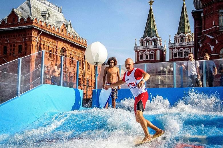 A man riding a flowboard on an artificial wave structure installed next to the Red Square and the Kremlin in Moscow on Tuesday. Various attractions were installed throughout the city to mark the 870th anniversary of Moscow.