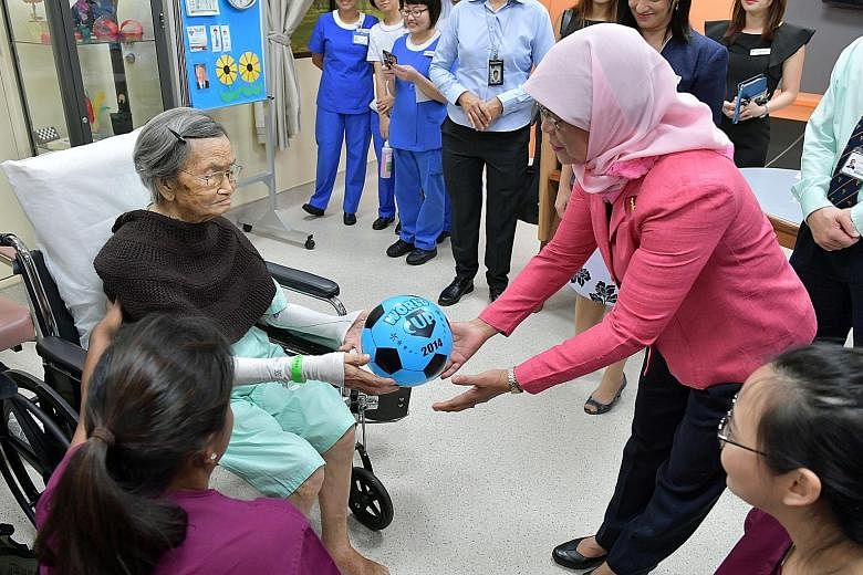 President Halimah Yacob interacting with 100-year-old Madam Liew Tim in the ward after her therapy session at NUH yesterday. Madam Halimah said she hoped her visit would demonstrate her support for healthcare workers, adding that they have "done very