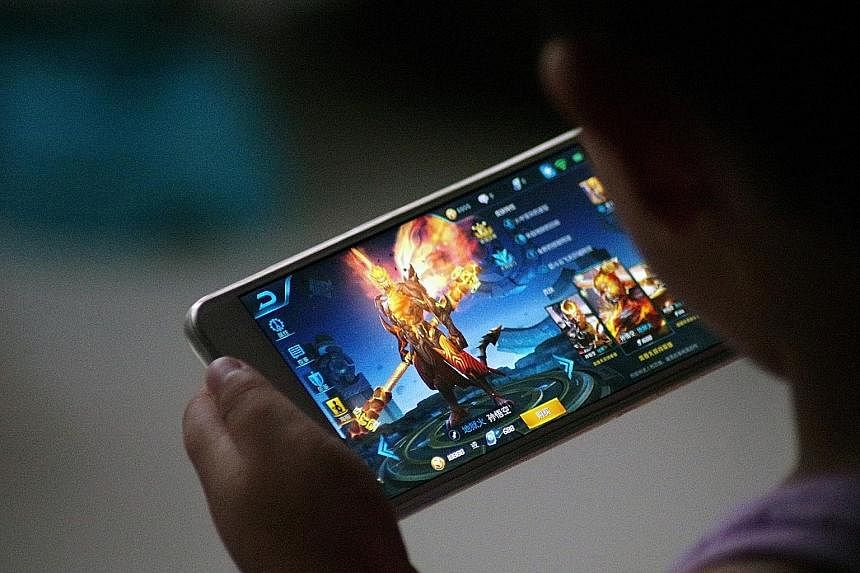 Tencent's Honour Of Kings has 200 million registered users in China alone. But it has been denounced as "poisonous" by Beijing after a teenager had a stroke after playing the game non-stop for 40 hours. A customer using a smartphone in front of the l