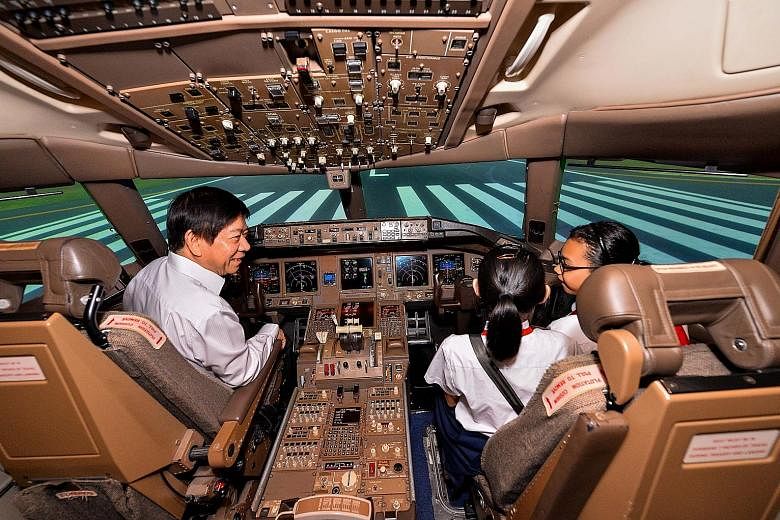 Transport Minister Khaw Boon Wan in a Boeing-777 flight simulator with beneficiaries of the Community Chest, who were given a tour of the SIA Training Centre in Changi yesterday. The Ministry of Transport and its statutory boards raised $1 million fo