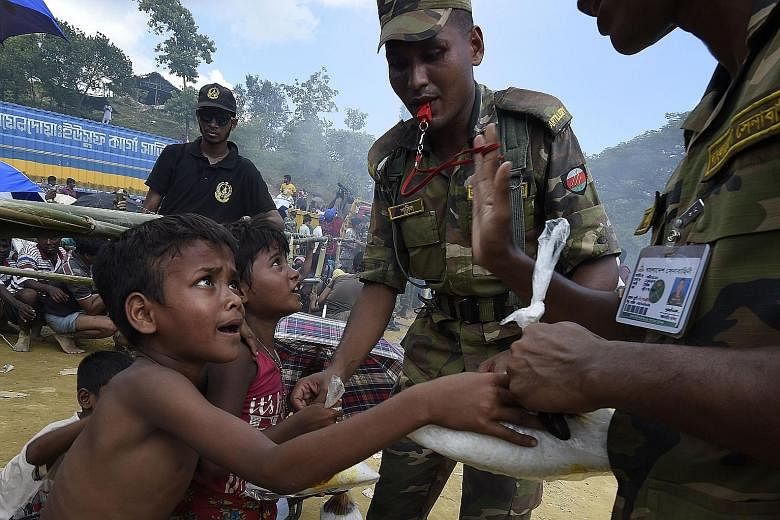 Above: Bangladeshi soldiers distributing rice to Rohingya refugees at a camp near Gumdhum yesterday. Left: A supporter of Myanmar leader Aung San Suu Kyi at a rally in Yangonon Sunday. Ms Suu Kyi has said the Myanmar government is taking measures to 