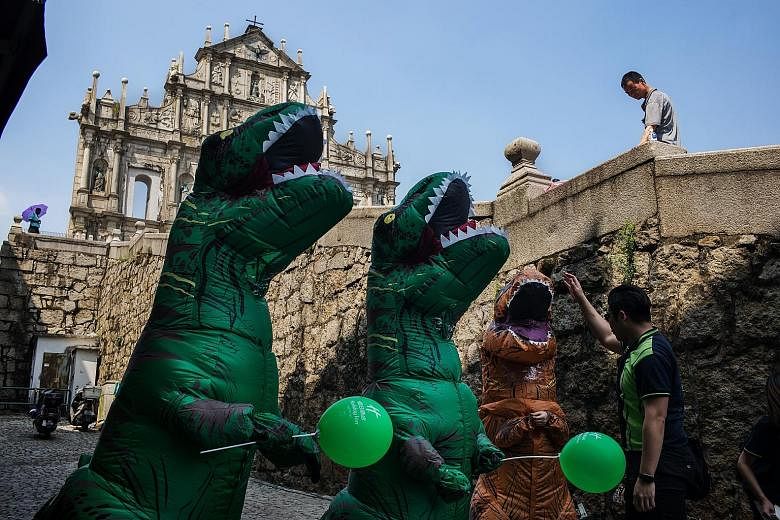 A man interacts with workers dressed in dinosaur costumes at the ruins of St Paul's Cathedral in Macau on Wednesday. Around 710 million Chinese will make trips within the country during the Golden Week holiday.