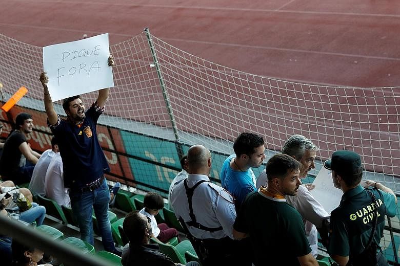 A Civil Guard officer removes a banner critical of Spain's Gerard Pique, while another spectator holds a sign that says: "Pique out" before a training session for the national team on Monday.