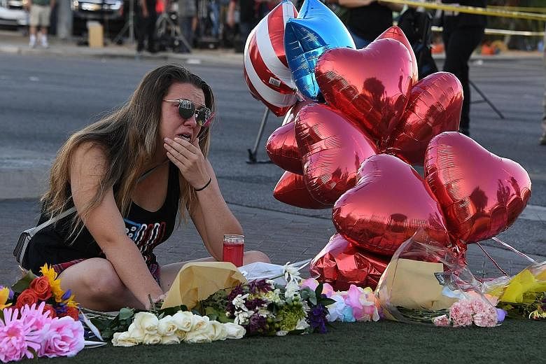 Ms Destiny Alvers, who attended the Route 91 country music festival and helped rescue her friend who was shot, grieving as she sat at a makeshift memorial on the Las Vegas Strip on Tuesday. Investigators are at a loss as to Stephen Paddock's motive f