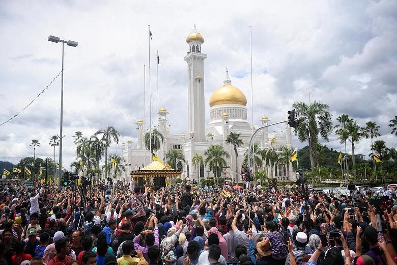 Above: Brunei Sultan Hassanal Bolkiah with his wife, Raja Isteri Pengiran Anak Hajah Saleha, at the throne hall of Istana Nurul Iman for the Golden Jubilee ceremony yesterday. Left: A huge crowd of people gathered in the streets of Bandar Seri Begawa
