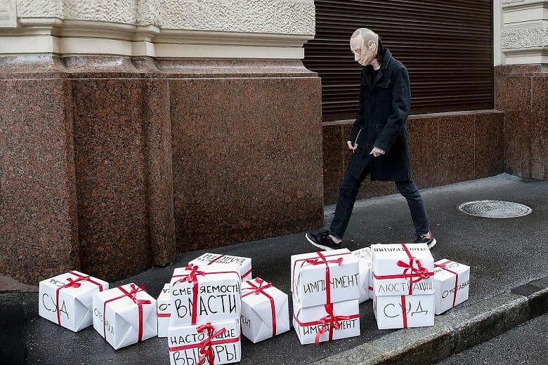 A protester wearing a Vladimir Putin mask walking past gift boxes with the words "trial", "resignation", "impeachment", "true election" and others during an event dedicated to the Russian President's 65th birthday in Moscow yesterday.