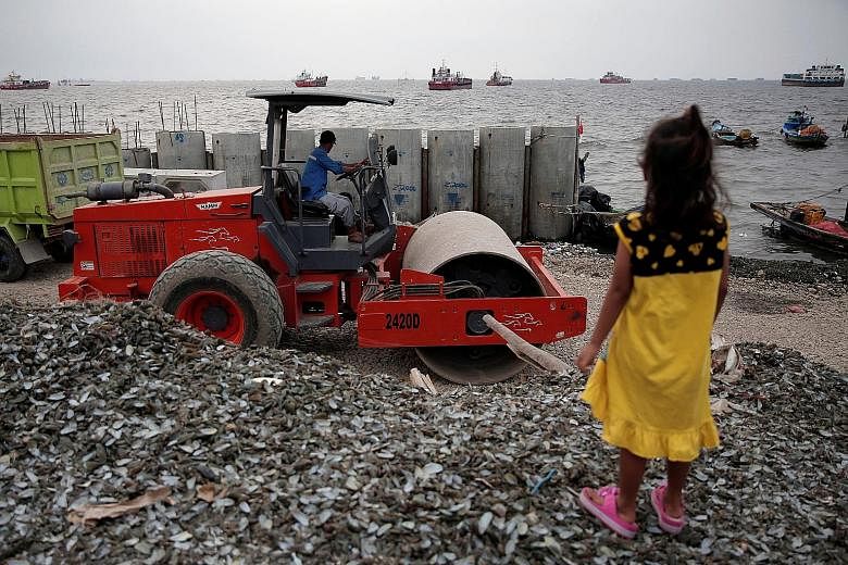 A child watching a worker operating heavy machinery for the construction of a concrete sea wall in North Jakarta in August. The low-lying Indonesian capital faces growing risks from rising sea levels, subsidence and annual flooding from more than a d