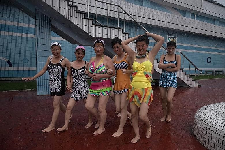 In Pyongyang, women wear brightly coloured swimsuits to the pool (top) and flowy dresses with high heels (above).