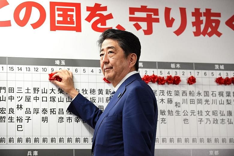 Japanese Prime Minister Shinzo Abe placing rosettes above the names of successful election candidates on a board at the LDP headquarters in Tokyo yesterday. The LDP and its coalition partner Komeito have secured 312 of the 465 Lower House seats, with