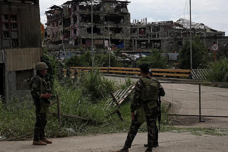 Above: Soldiers standing guard after troops cleared the area of pro-ISIS militants inside the war-torn area of Saduc Proper in Marawi, in the southern Philippines yesterday. Left: A local government worker putting up a sign in the same area in Marawi