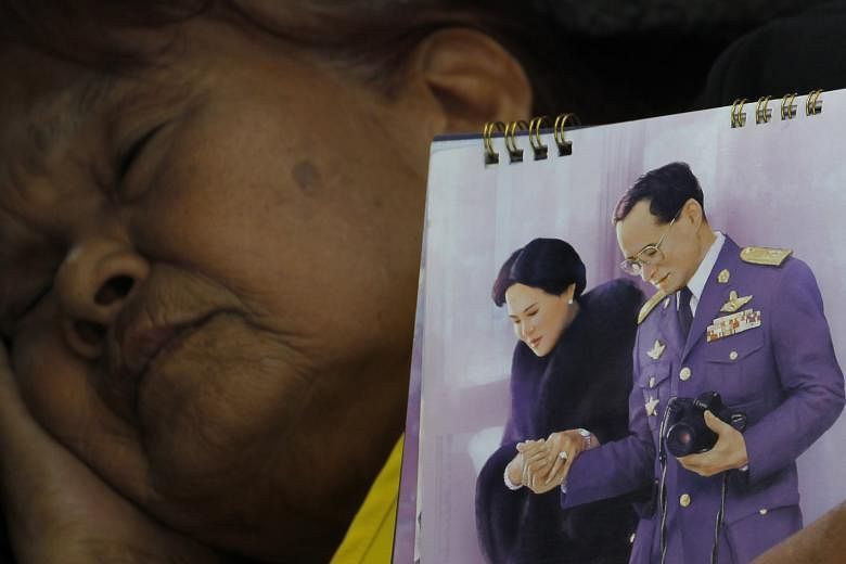 A mourner holding a portrait of King Bhumibol and Queen Sirikit near the Grand Palace yesterday.