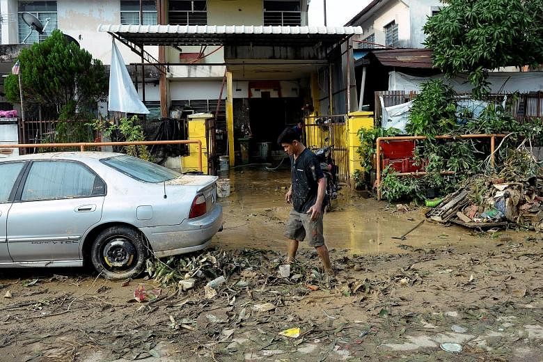 The view from a Malaysian Maritime Enforcement Agency helicopter shows the extent of the flood damage in a residential area in Penang yesterday. The number of evacuees in the state rose to 5,478. A resident making his way through a mud-filled road in