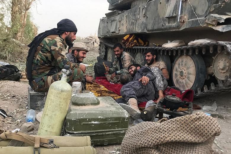 Syrian government forces resting beside an armoured vehicle in Deir Ezzor, sited on the western bank of the Euphrates River, on Sunday, after retaking the city from ISIS militants.