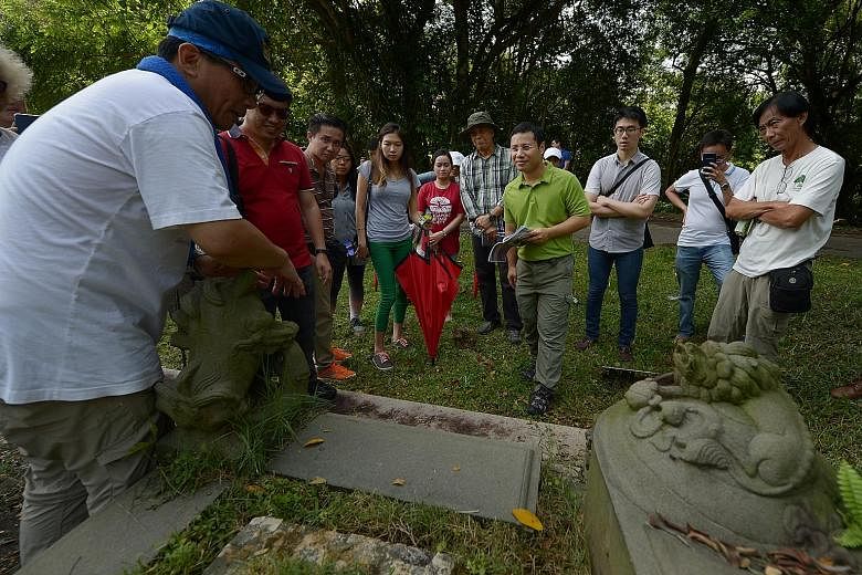 Bukit Brown volunteer Fabian Tee (left), 50, showing Social and Family Development Minister Desmond Lee (in green) yesterday the details of a tomb at the launch of the trail at Bukit Brown Cemetery.