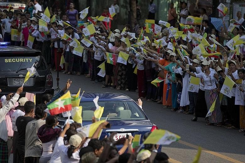 Above: A girl dressed in traditional dress embracing Pope Francis on his arrival. Left: The Pope waving from his car window at crowds gathered in Yangon. Thousands travelled across the country to see him.