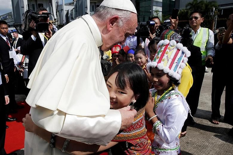 Above: A girl dressed in traditional dress embracing Pope Francis on his arrival. Left: The Pope waving from his car window at crowds gathered in Yangon. Thousands travelled across the country to see him.