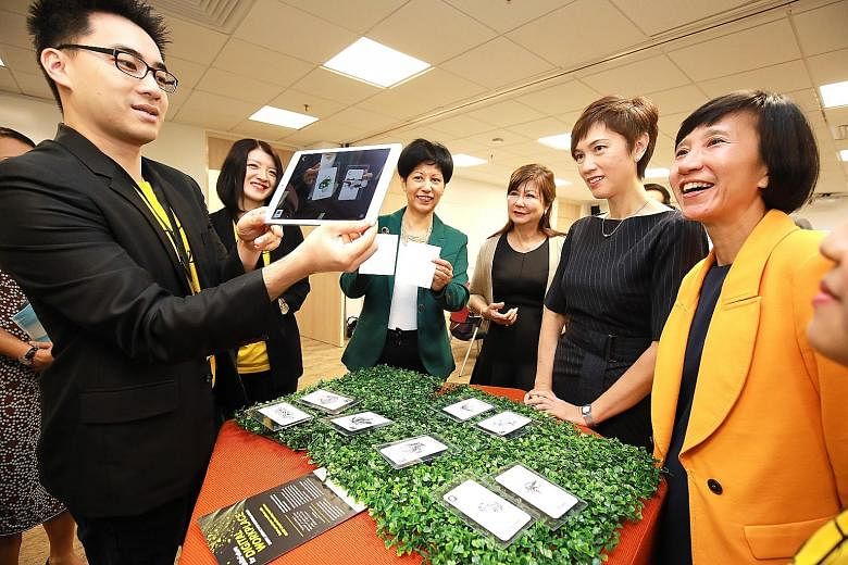 Ms Josephine Teo (second from right) and Ms Indranee Rajah (third from left) watching a demonstration of augmented reality technology, which is part of the Professional Conversion Programme, together with United Overseas Bank's head of group human re