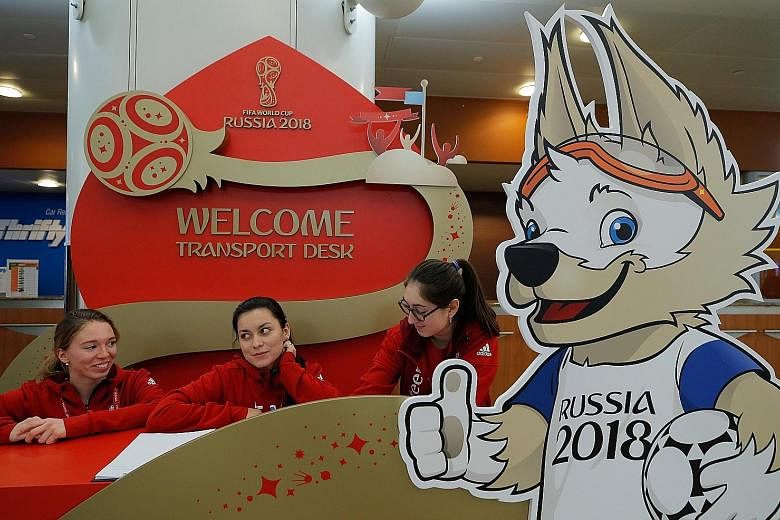 Staff await arrivals at the Sheremetyevo International Airport just outside Moscow for the World Cup Finals draw. Next to them is an ad board of Zabivaka, the competition's wolf mascot.