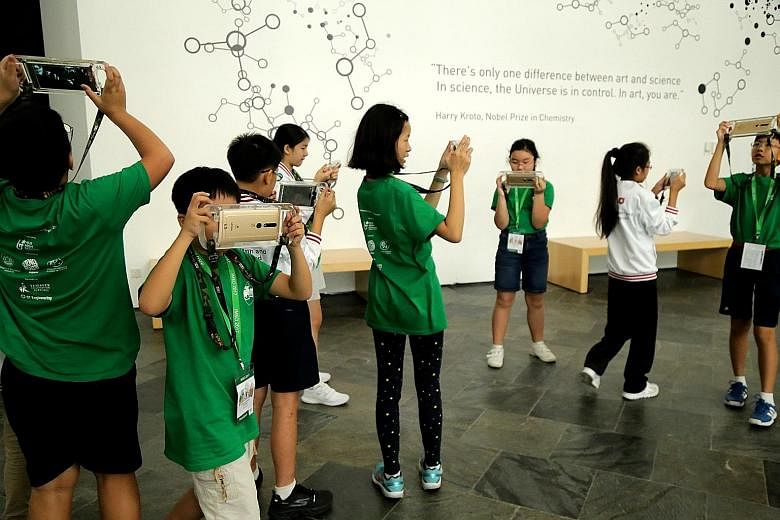 Team Singapore pupils testing out augmented reality on mobile devices during the Into The World experience at the ArtScience Museum. A student from the NUS High School of Mathematics and Science showing the girls from Team Iran how facilities in one 