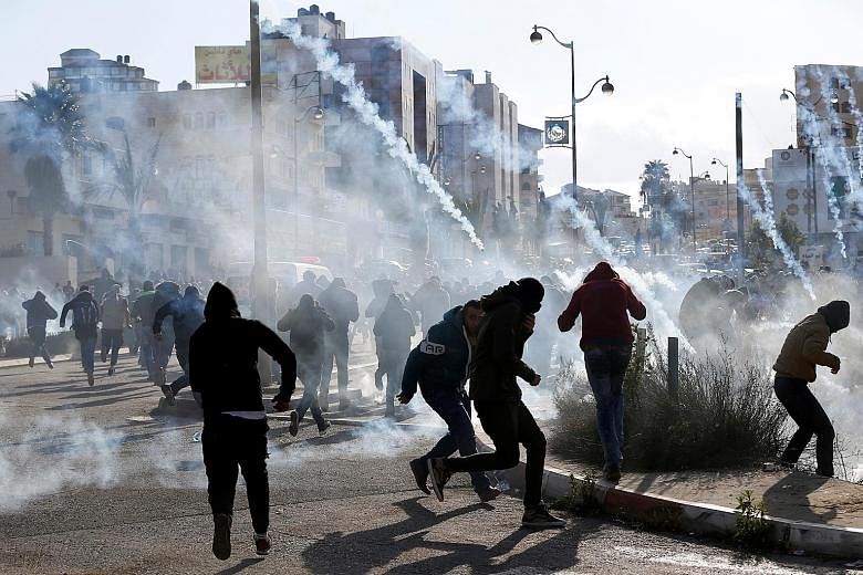 Above: Palestinian protesters running from tear gas fired by Israeli troops yesterday during clashes at a protest against the US' move to recognise Jerusalem as the Israeli capital, near the West Bank city of Ramallah. Below: Mr Trump holding the pro