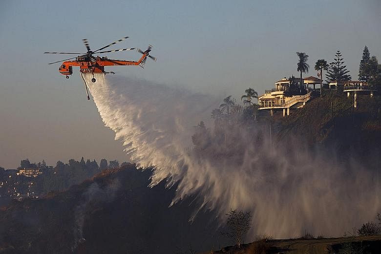 A firefighting helicopter dropping water over the Bel-Air neighbourhood of Los Angeles, California, on Wednesday in an effort to douse a blaze. The raging wildfires have threatened multimillion-dollar mansions with blazes that have already forced mor