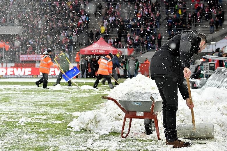 GERMANY: Ground staff removing snow (right) from the pitch prior to the German Bundesliga football match between FC Cologne and SC Freiburg in Cologne on Saturday. BRITAIN: A sign (left) alerting drivers to road closures near Wrexham, north Wales, ye