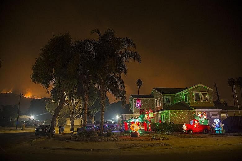 Left: Christmas decorations illuminating a house as the growing Thomas Fire advances towards the Santa Barbara County seaside communities on Sunday. Above: People watching the Thomas Fire from a distance in Carpinteria, California.