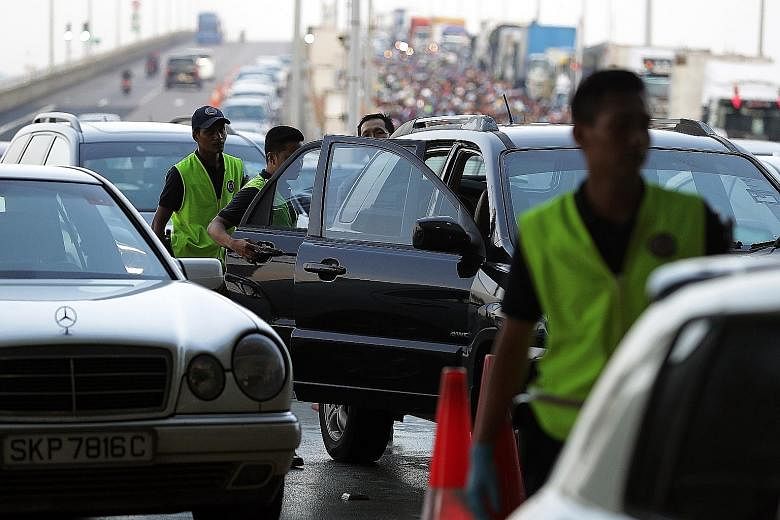 ICA officers conducting checks at Tuas Checkpoint yesterday. About 430,000 people - 30,000 more than usual - are expected to clear the two checkpoints daily during the December school holiday period.