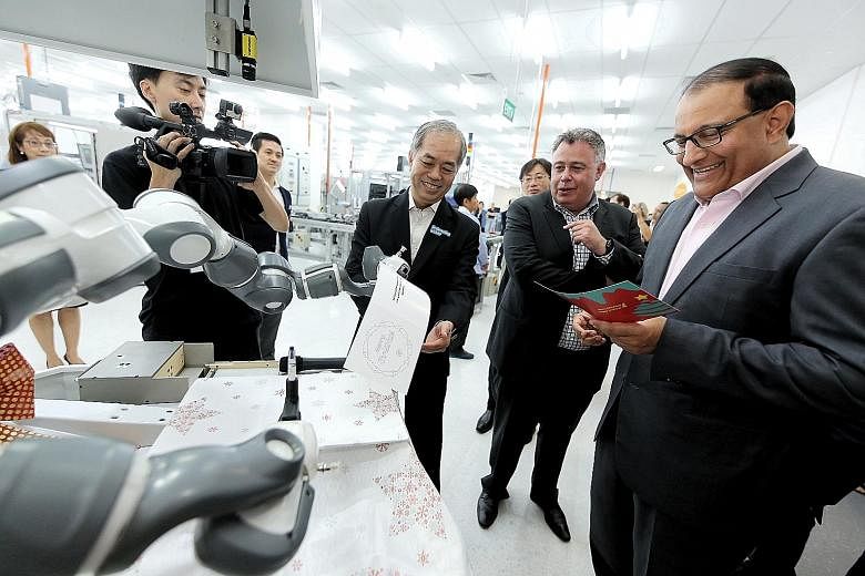 Minister S. Iswaran receiving a card with greetings written by a robotic arm at HP's first Smart Manufacturing Applications and Research Centre. With him are Mr Dominic Chew, HP director of operations, supplies operations, and Mr Dion Weisler, HP pre