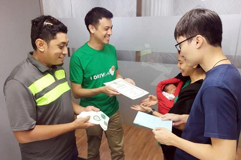 Grab driver Mohammad Fazli Omar and GrabCar Singapore head Andrew Chan presenting Mr Reuben Chow and Madam Cindy Lim with a Grab voucher worth $8,000, and a special Grab garment for newborn baby Elora-Fae.