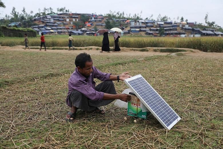 A Rohingya refugee using a solar panel to charge his mobile phone at the Palong Khali refugee camp in Cox's Bazar. Some refugees relied on their phones for information on safe routes to take while fleeing Myanmar.