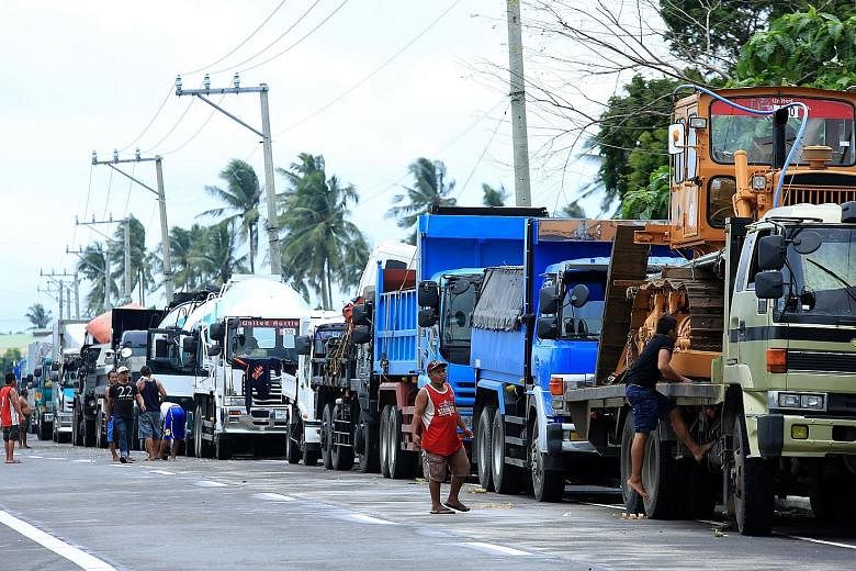 A long line of vehicles on a highway heading to the port in Matnog, Sorsogon, yesterday. Ferry services remained suspended, stranding thousands of people heading home for Christmas. A resident stands amid the damage after Tropical Storm Kai-Tak yeste