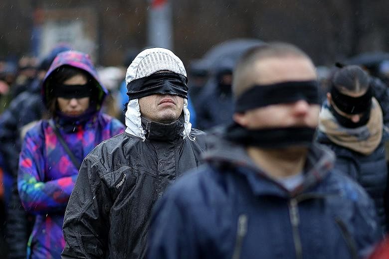 Romanians standing in silent protest, black scarves and tapes covering their eyes and mouths, outside the government headquarters in Bucharest on Sunday. About a hundred people gathered despite the rain for the silent flash mob named "Romania Silence