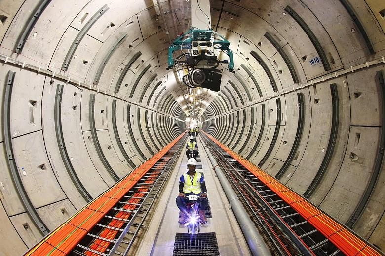 SP Group staff riding electric bicycles yesterday in the tunnel network of the Underground Transmission Cable Tunnel Project. Above them is a prototype model of an automatic inspection vehicle, the final version of which will be used to monitor the t