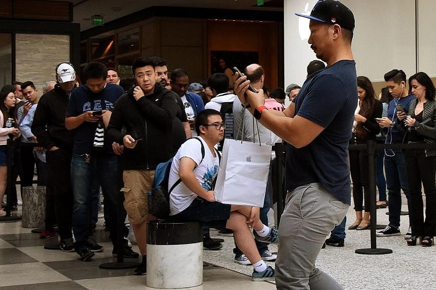 A man leaving an Apple Store in Los Angeles with his new iPhone X as others wait to buy theirs on Nov 3, when it was released. Analysts have cut iPhone X shipment projections for the first quarter of next year.