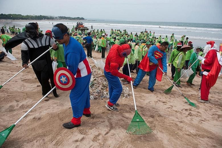Workers, wearing superhero costumes to attract tourists, sweeping up garbage at Kuta beach in Bali, Indonesia, yesterday. Some 400 cleaners were deployed for the operation, with eight of them dressing up as superheroes such as Superman, Batman and Th