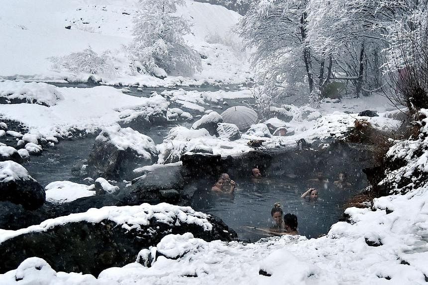 Amid the wintry chill, a child in Riedlingen, in southern Germany, enjoys a bit of fun in the snow during the festive season. Above: People braving the cold to take a dip in the natural hot water springs of Bormio, in the north of Italy, on Wednesday
