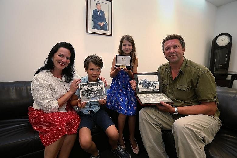 Ms Victoria Humble-White with her children, Oliver and Rosa, and Mr Tim Proffitt-White. They are holding up photos of Mr Chris Proffitt-White and a medal presented to him by Boon Siew Limited.